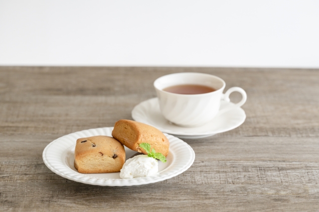 スコーンと紅茶のセット。白いカップに入った紅茶と、ホイップクリーム添えのスコーンが木目テーブルに置かれている。