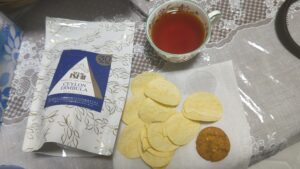 成城石井のセイロン・ディンブラ。ティーバッグパックとカップの紅茶、ポテトチップスとクッキーを添えたテーブル
